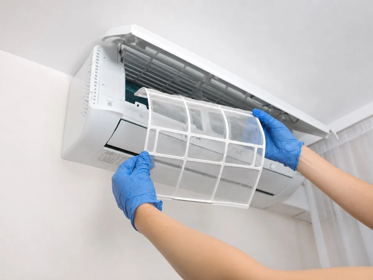 Manos con guantes sacando el filtro de un split para limpiarlo
